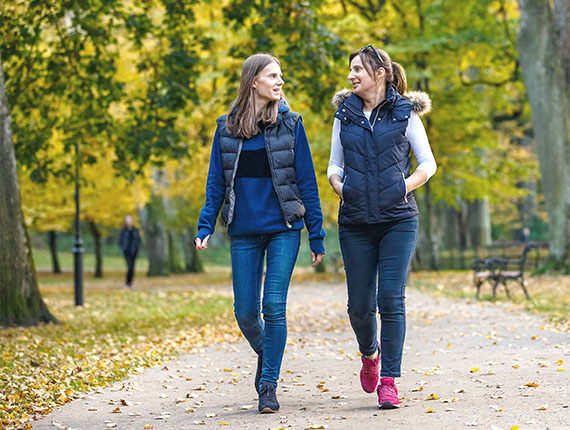 Two women are walking together in a park laughing and joking with each other