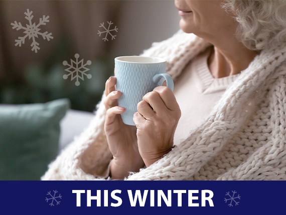 Older lady holding cup of hot drink while snuggled in a blanket