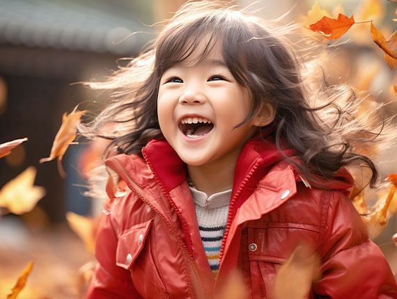 A small happy girl in a red coat playing in the autumn leaves on the ground